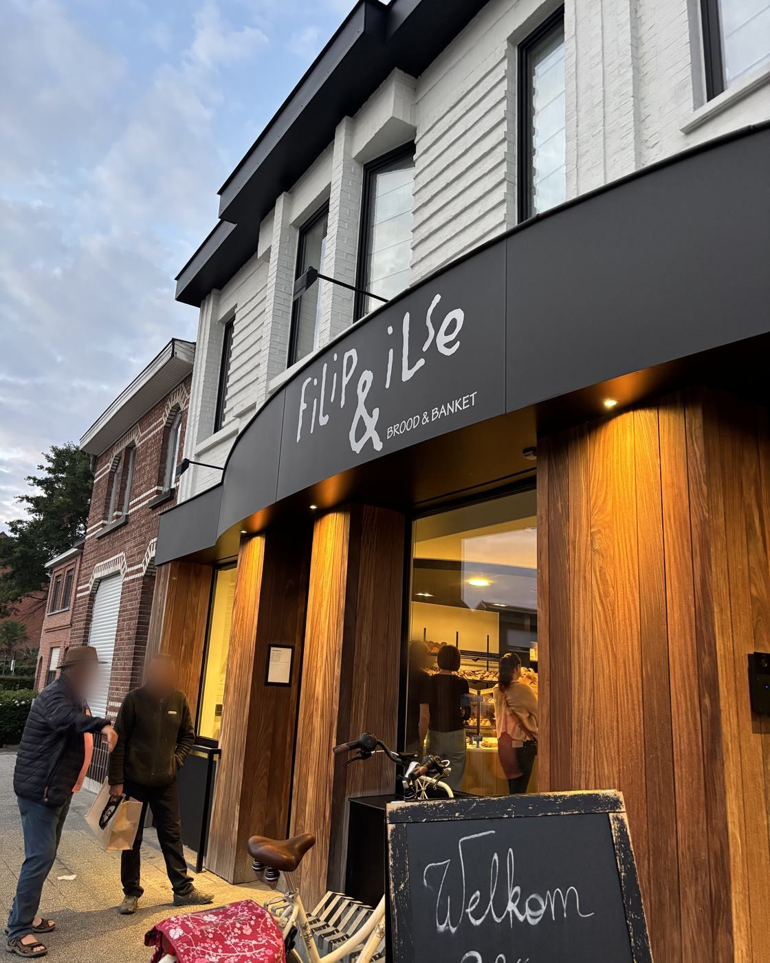 De voorgevel van bakkerij Filip & Ilse aan de Stationsstraat in Kemzeke, met houten gevel en warme verlichting